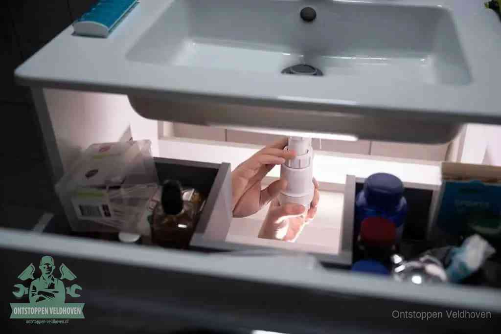 Een pompfles met zeep boven een wastafel, de heet water en afwasmiddel-methode om een vetprop in de afvoer los te maken in Veldhoven