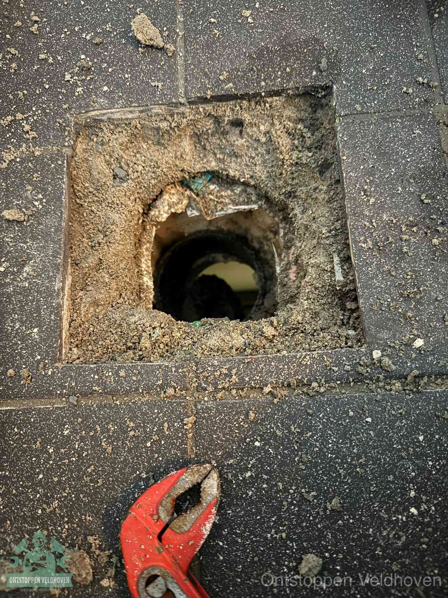 Een geopend rioolputje in een betontegelvloer met losgemaakt rooster en een zichtbare ronde afvoerbuis, het achterhalen waar de afvoerverstopping zit in Veldhoven