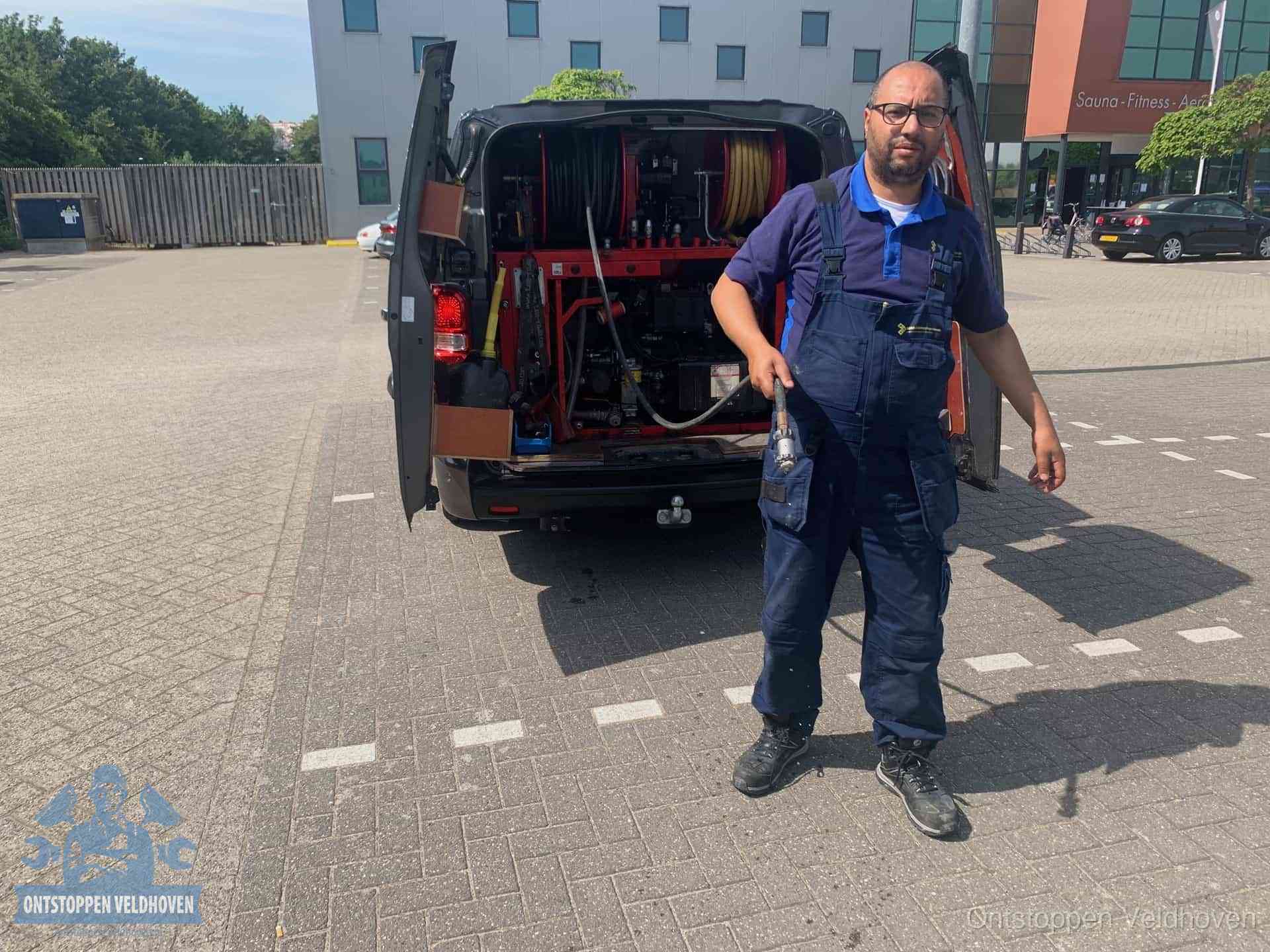 Een monteur bij zijn bestelbus met een hogedruk- en rioolreinigingsunit, klaar om de oorzaak van terugkerende wc-verstoppingen aan te pakken in Veldhoven