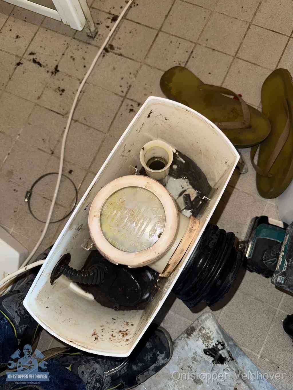 Een gedemonteerde toiletpot op de vloer met ontstoppingsveer en gereedschap ernaast, het verwijderen van een vastzittend voorwerp uit de wc in Veldhoven